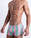 Side view of a male model wearing men’s THE KEN (MALIBU EDITION) sexy men’s swimming shorts by BANG! Clothes in Miami, featuring pastel pink and aqua blue stripes.