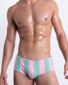 Frontal view of a male model wearing THE KEN (MALIBU EDITION) Swim Sunga, premium bikini-style bottoms in pink and light aqua-colored stripes inspired by the styles seen worn by Ryan Gosling as Ken, in the Barbie movie. Designed by BANG! Clothes, a men’s beachwear brand from Miami.