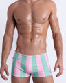 Frontal view of a male model wearing THE KEN (MALIBU EDITION) Swim Trunks with a zippered mini pocket, premium swimwear in pink and light aqua-colored stripes inspired by the styles seen worn by Ryan Gosling as Ken, in the Barbie movie. Designed by BANG! Clothes, a men’s beachwear brand from Miami.