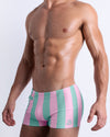 Side view of a male model wearing men’s THE KEN (MALIBU EDITION) sexy Summer beach trunks by BANG! Clothes in Miami, featuring pastel pink and aqua-colored stripes.