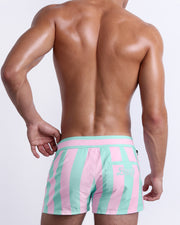 Back view of a male model wearing men’s THE KEN (MALIBU EDITION) Beach Shorts swimsuit by BANG! Clothes in Miami, featuring pastel pink and aqua colored stripes. 