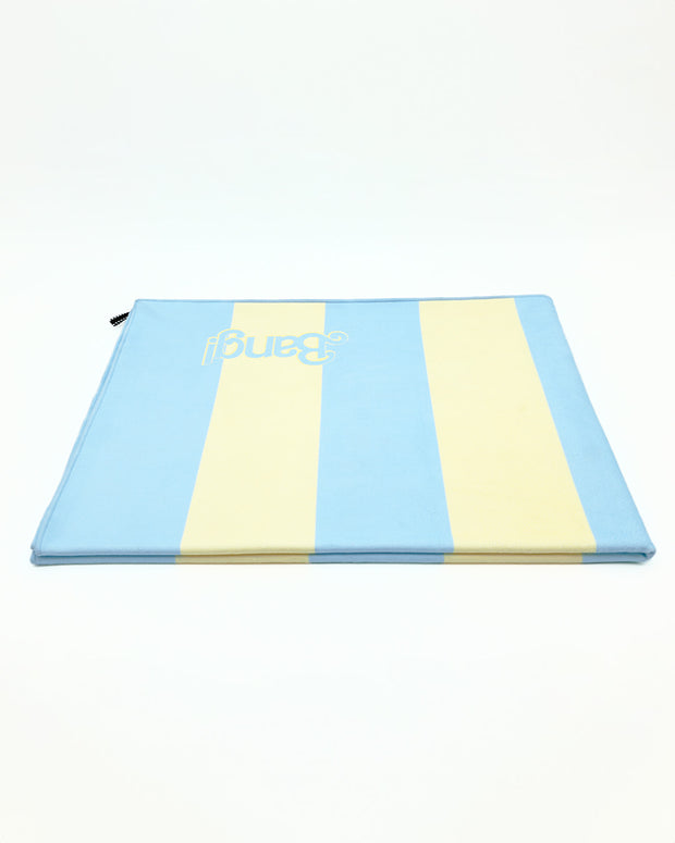 Image of the Ken (Miami Edition) folded quick-dry microfiber beach towel. This soft towel is in a striped pastel yellow and blue design with the BANG! logo and built-in hanging loop.