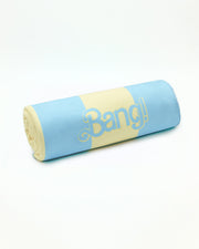 A rolled-up THE KEN (MIAMI EDITION) quick-dry microfiber towel. Inspired by the Barbie movie, it features SoBe/Art-Deco pastels in blue and pastel yellow stripes, designed by BANG! Clothes in Miami.