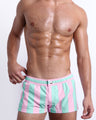 Male model wearing THE KEN (MALIBU EDITION) square leg swim shorts, premium swimwear in pink and light aqua-colored stripes inspired by the styles seen worn by Ryan Gosling as Ken, in the Barbie movie. Designed by BANG! Clothes, a men’s beachwear brand from Miami.