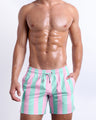 Male model wearing THE KEN (MALIBU EDITION), premium swimwear in pink and light aqua-colored stripes inspired by the styles seen worn by Ryan Gosling as Ken, in the Barbie movie. Designed by BANG! Clothes, a men’s beachwear brand from Miami.