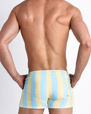 Back view of male model wearing the THE KEN (MIAMI EDITION) beach trunks featuring cool light blue color and pastel yellow stripes for men by BANG! Miami. Inspired by the Barbie movie SoBe/Art-Deco-inspired.