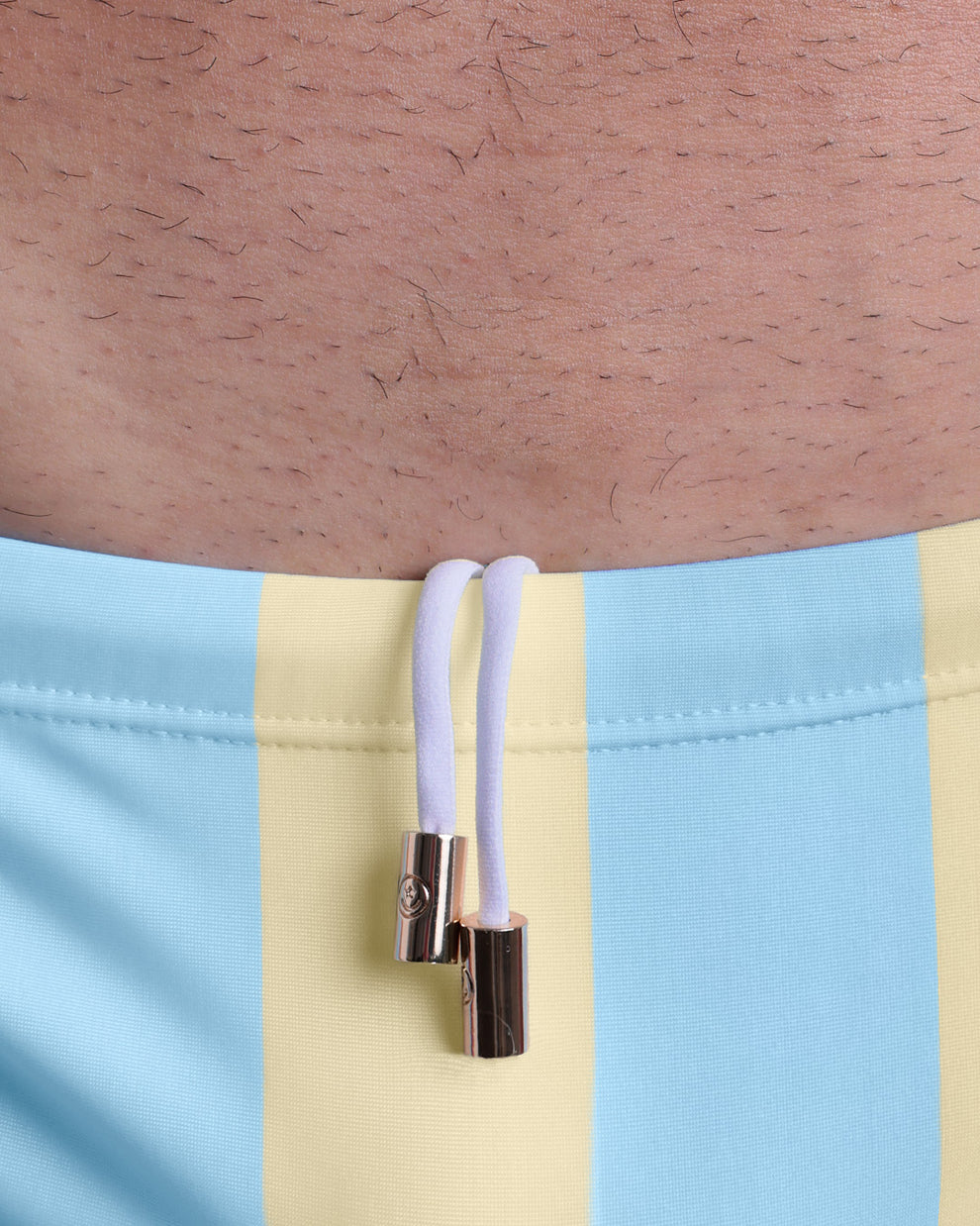 Close-up view of men’s summer Swim Sunga by BANG! clothing brand, showing white cord with custom branded golden cord ends, and matching custom eyelet trims in gold.