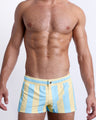 Male model wearing THE KEN (MIAMI EDITION) square leg swim shorts, premium swimwear in yellow and light blue-colored stripes inspired by the styles seen worn by Ryan Gosling as Ken, in the Barbie movie. Designed by BANG! Clothes, a men’s beachwear brand from Miami.