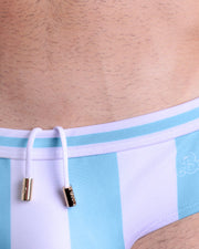 Close-up view of the THE KEN (MYKONOS EDITION) men’s drawstring briefs showing white cord with custom branded golden cord ends, and matching custom eyelet trims in gold.