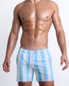 Male model wearing THE KEN (MYKONOS EDITION), premium swimwear in white and light blue-colored stripes inspired by the styles seen worn by Ryan Gosling as Ken, in the Barbie movie. Designed by BANG! Clothes, a men’s beachwear brand from Miami.