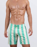 Frontal view of a male model wearing the THE KEN (TULUM EDITION) - Flex Boardshorts by BANG! Miami. These premium swimming boardshorts feature a striking mint-green and cream striped design, side panels and waistband, deep zippered pockets, and a dual-type 