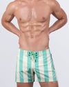 Frontal view of a male model wearing The Ken (Tulum Edition) Flex Shorts for men by BANG! Miami. These premium mid-length swim shorts feature a fresh mint green and cream vertical stripe pattern, a lace-up front closure with gold-tone aglets, and a contoured fit that blends vintage charm with modern beachwear look.
