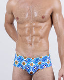 Male model wearing THE TILE IS HIGH swim brief by DC2 Miami – men's designer swimwear with Mediterranean tile-inspired print in blue, orange, and white.