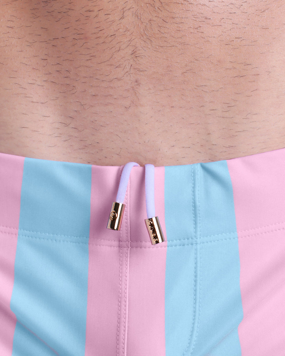 Close-up view of trims of THE KEN (IBIZA EDITION) waistband drawstring, with white cord and custom branded golden cord-ends, and matching custom eyelet trims in gold.
