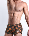 Left side view of a masculine model wearing men’s swimwear featuring a black and brown Tiger Pop Art Monogram print with official logo of BANG! Brand in white.