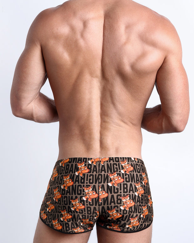 Back view of a male model wearing TIGER HEARTS men’s swim shorts in brown with orange tigers holding a heart pop artwork by the Bang! Clothes brand of men&