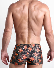 Back view of a Male model wearing swim trunks for men in brown with orange tigers holding a heart pop artwork by the Bang! Clothes brand of men's beachwear.