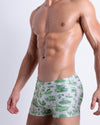 Side view of muscular male model wearing TOILE DE MIAMI (GREEN) Summer swimming trunks swimsuit for the beach in a stylish white color with green Toile de Jouy print for men is designed by BANG! Clothes in Miami.