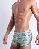 Side view of muscular male model wearing TOILE DE MIAMI (GREEN) Summer swimming trunks swimsuit for the beach in a stylish white color with green Toile de Jouy print for men is designed by BANG! Clothes in Miami.