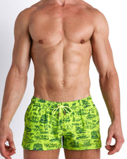 Front view of model wearing the TOILE DE MIAMI (NEON GREEN/BLUE) men’s beach shorts in lime green with blue Toile De Jouy art by the Bang! Clothes brand of men's beachwear from Miami.