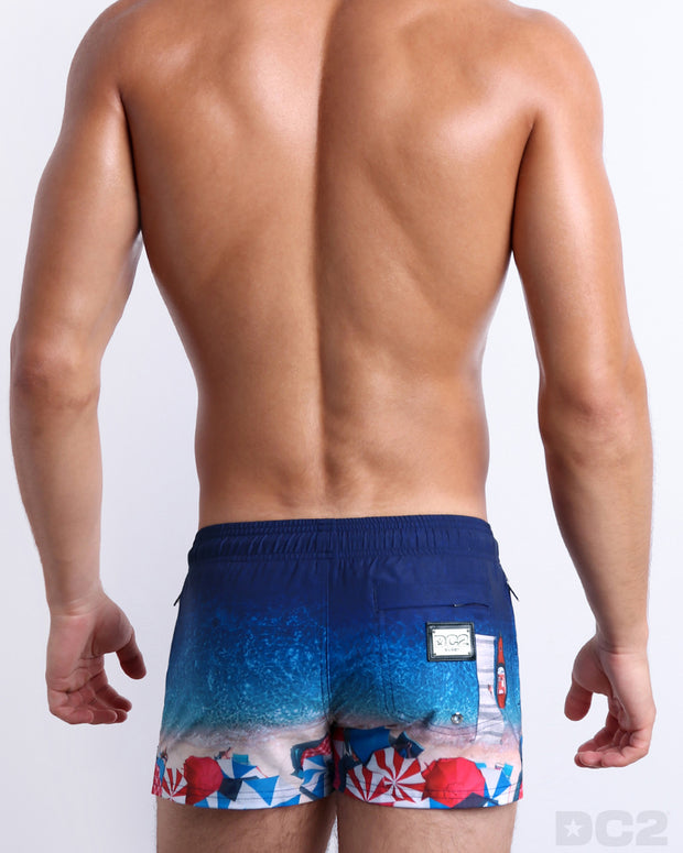 Male model wearing a men’s UNDER A UMBRELLA beach Poolside Shorts swimsuit, complete with a back zippered pocket, designed by DC2 a capsule brand by BANG! Clothes based in Miami.
