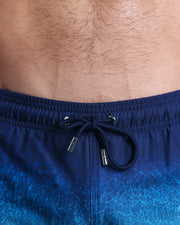 Close-up view of the UNDER MY UMBRELLA men’s summer shorts, showing dark blue cord with custom branded silver cord ends, and matching custom eyelet trims in silver.