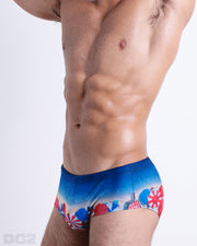 Side view of muscular male model wearing UNDER MY UMBRELLA Summer swimming Sunga. This swimsuit featured a photorealistic beach scene print designed by DC2 a brand based in Miami.