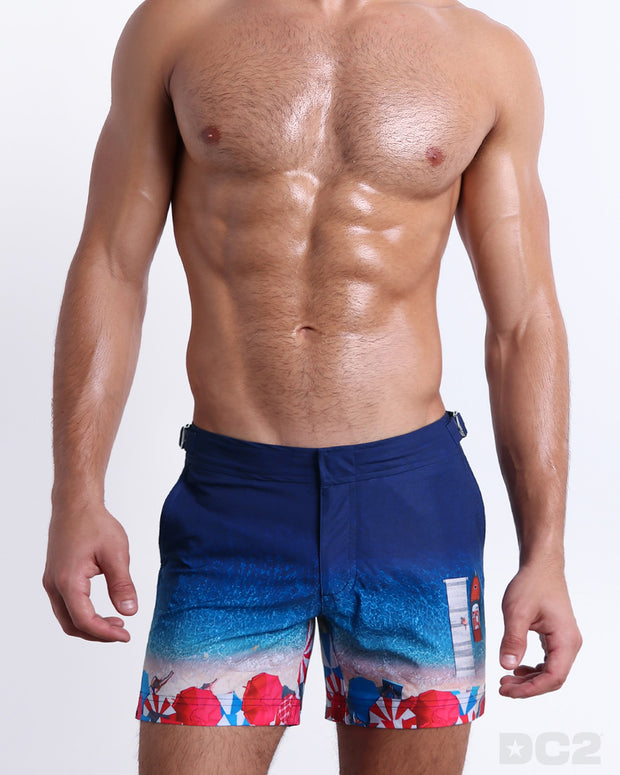 Male model wearing UNDER MY UMBRELLA Tailored Shorts, in a ombre print of a Miami beach scene for men. These premium quality swimwear bottoms are DC2 by BANG! Clothes, a men’s beachwear brand from Miami.