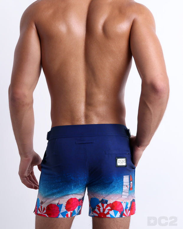 Male model wearing a men’s UNDER A UMBRELLA beach Tailored Shorts swimsuit, complete with a back pocket, designed by DC2 a capsule brand by BANG! Clothes based in Miami.