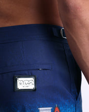 Close-up view of the UMBRELLA MY UMBRELLA men’s swimwear, showing custom-branded silver logo plaque.