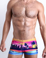 Frontal view of a sexy male model wearing men's swimsuit with mini pockets in UNDER A NEON SKY in pink & orange sunset skyline print designed by the Bang! Menswear brand from Miami.