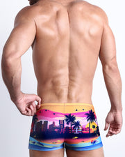 Back view of a Male model wearing swim trunks for men in a pop color with the miami sunset skyline by the Bang! Clothes brand of men's beachwear.
