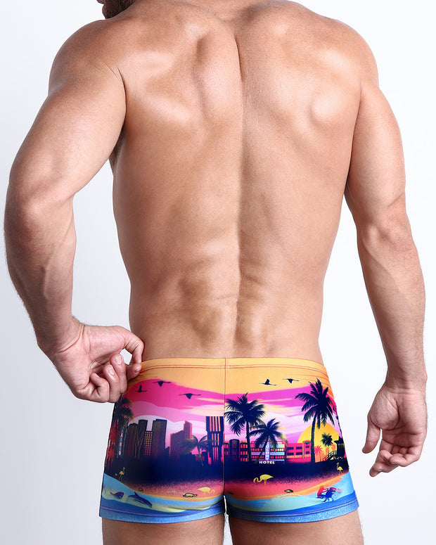 Back view of a Male model wearing swim trunks for men in a pop color with the miami sunset skyline by the Bang! Clothes brand of men&