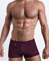 DC2 VERY BERRY — model wearing square-cut Swim Trunks in deep berry hue, featuring a skin-hugging silhouette.