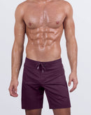 Frontal view of a male model wearing the VERY BERRY Flex Boardshorts for men by DC2 Miami. These stylish boardshorts feature a deep berry hue, a hybrid flat-front waistband with an elasticated back, an adjustable drawstring, and a longer leg cut, designed for a comfortable fit in and out of the water.