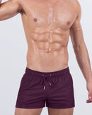 Model wearing VERY BERRY poolside shorts in a bold berry purple. Stylish swimwear with an athletic fit and adjustable drawstring waist, ideal for poolside lounging.