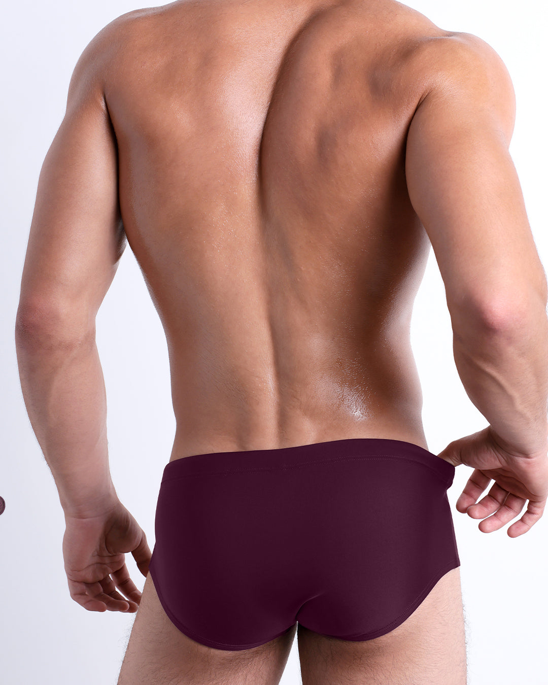 Back view of male model wearing the VERY BERRY beach Brazilian Sunga swimwear for men by BANG! Miami in a solid red wine color.