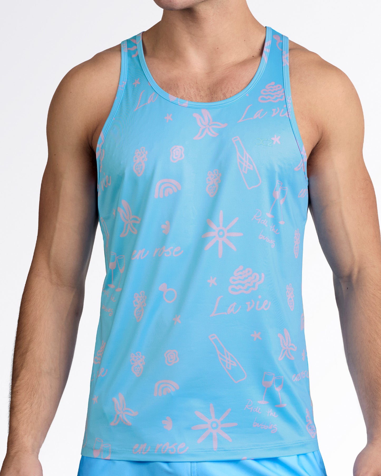 DC2 Viva La Vida (En Rose) Gym Tank Top — model wearing aqua blue men’s tank featuring soft pink graphic illustrations including sun, waves, champagne bottle, and “La vie” script.