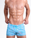 DC2 Viva La Vida (En Rose) Poolside Shorts — model wearing light blue swim shorts featuring a playful pink graphic print with icons and phrases like “La vie” and “en rose,” designed with an elastic waistband and adjustable drawstring for a comfortable poolside fit.