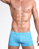 DC2 Viva La Vida (En Rose) — model wearing Viva La Vida Swim Trunk featuring a turquoise blue base with soft pink illustrated icons and handwritten “en rose” script detailing throughout.