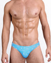 DC2 Viva La Vida (En Rose) — model wearing Viva La Vida (En Rose) Swim Mini Brief featuring a turquoise base with soft pink graphic icons and “La vie en rose” script print.