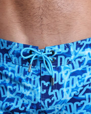 Close-up view of men’s summer Flex Boardshorts by DC2 clothing brand, showing  blue color cord with custom-branded silver cord ends, and matching custom eyelet trims in black.