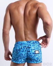 Back view of male model wearing men’s WET beach Mini Shorts swimsuit featuring a monogram print of the DC2 logo print, complete with a back pocket, designed by DC2.