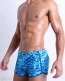 Side view of a male model wearing men’s WET sexy men’s swimming shorts, in a monogram print of the DC2 logo print by DC2 a brand based in Miami.