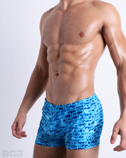 Side view of muscular male model wearing WET Summer swimming Trunks. This swimsuit has a stylish monogram print of the DC2 logo in multiple shades of blue for men made by DC2 a brand based in Miami.