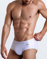 Left side view of a masculine model wearing men’s swimwear in white color featuring a side pocket with official logo of BANG! Brand.