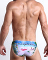 Back view of a model wearing WISH YOU WERE HERE men’s beach mini-brief featuring a colorful Miami art deco architecture inspired artwork made by the Bang! Miami official brand of men's swimwear.