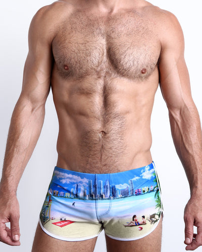 Frontal view of a sexy male model wearing men’s WISH YOU WERE HERE swimsuit Miami Beach skyline art by the Bang! Menswear brand from Miami.