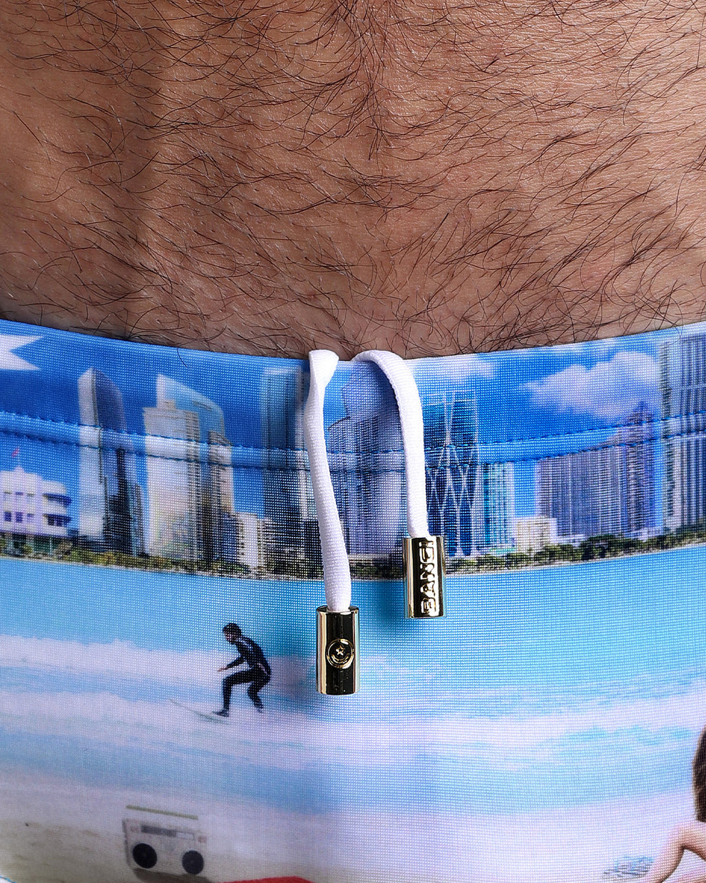 Close-up view of the WISH YOU WERE HERE Swim Sunga mens swimsuit inspired by the Miami Beach skyline artwork with an internal drawstring cord in white showing custom branded golden buttons by BANG! clothing brand.