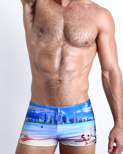 Frontal view of a sexy male model wearing men's swimsuit with mini pockets in WISH YOU WERE HERE featuring a colorful Miami art deco architecture inspired artwork designed by the Bang! Menswear brand from Miami.